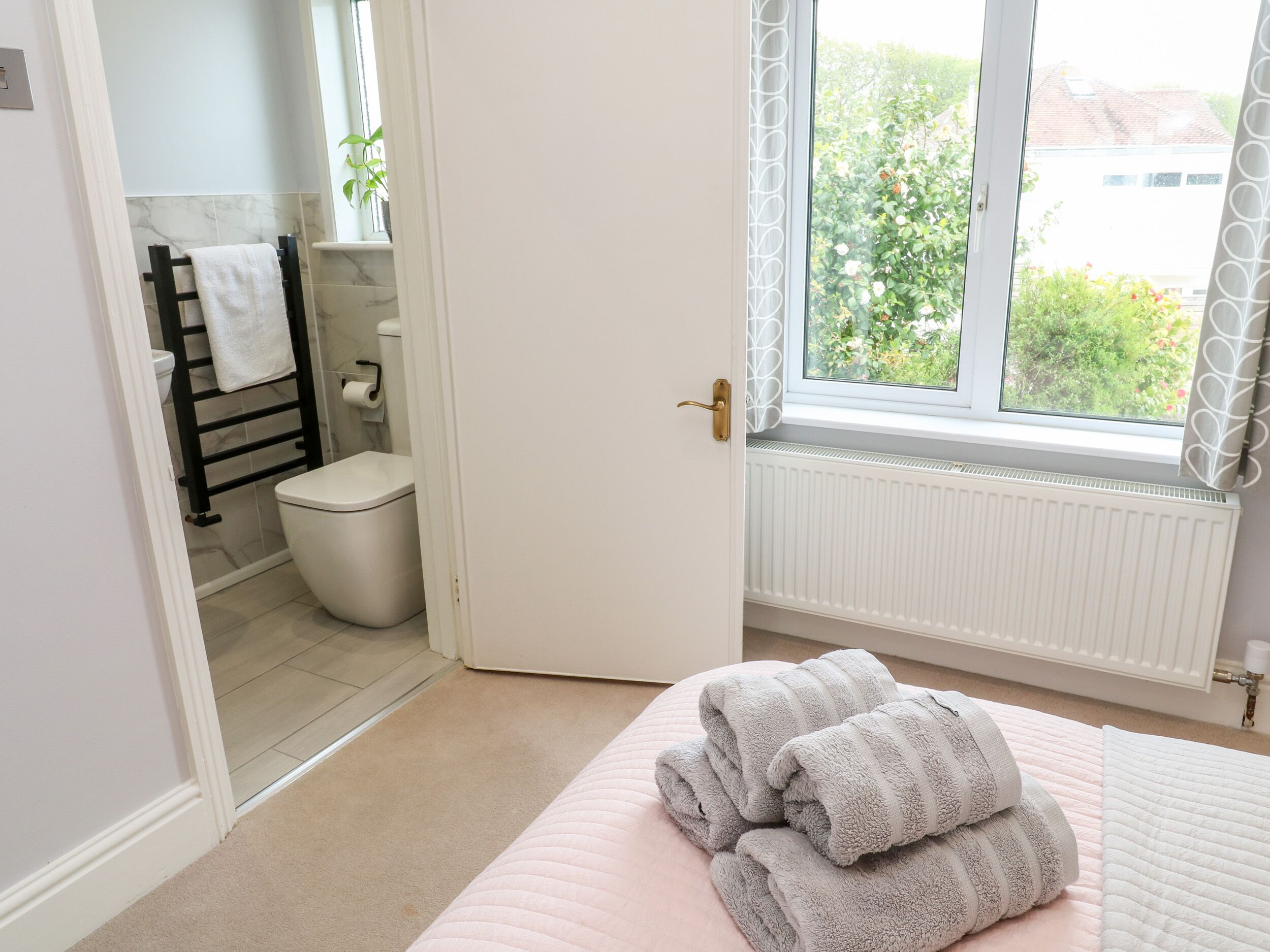 Een badkamer met toilet, handdoekrek en raam met uitzicht op groen.