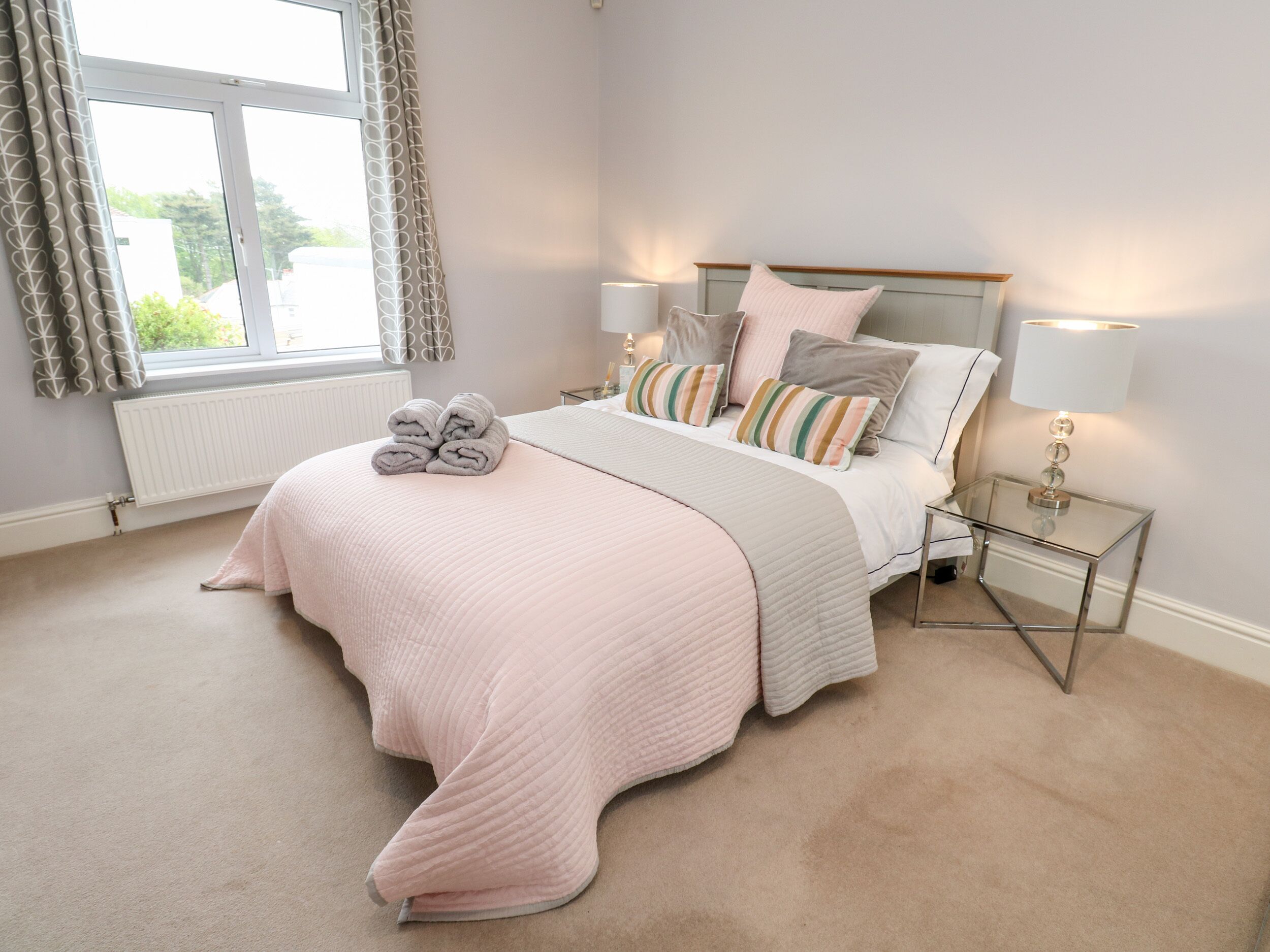 A bedroom with a bed, two bedside tables, a window with curtains, and a radiator.