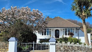 A white house with a dark brown roof, a stone wall, and a metal gate. - Robin Hill (St Austell)