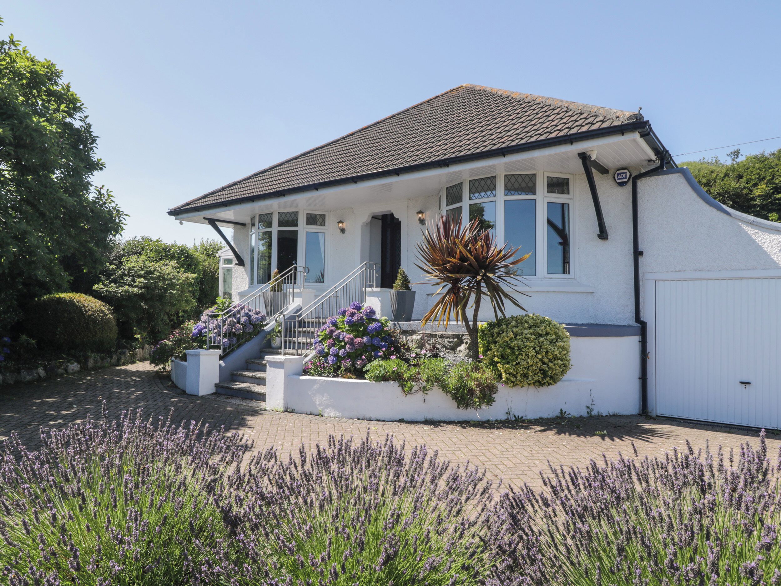 Een wit huis met een pannendak, een veranda met treden en een tuin met lavendel.