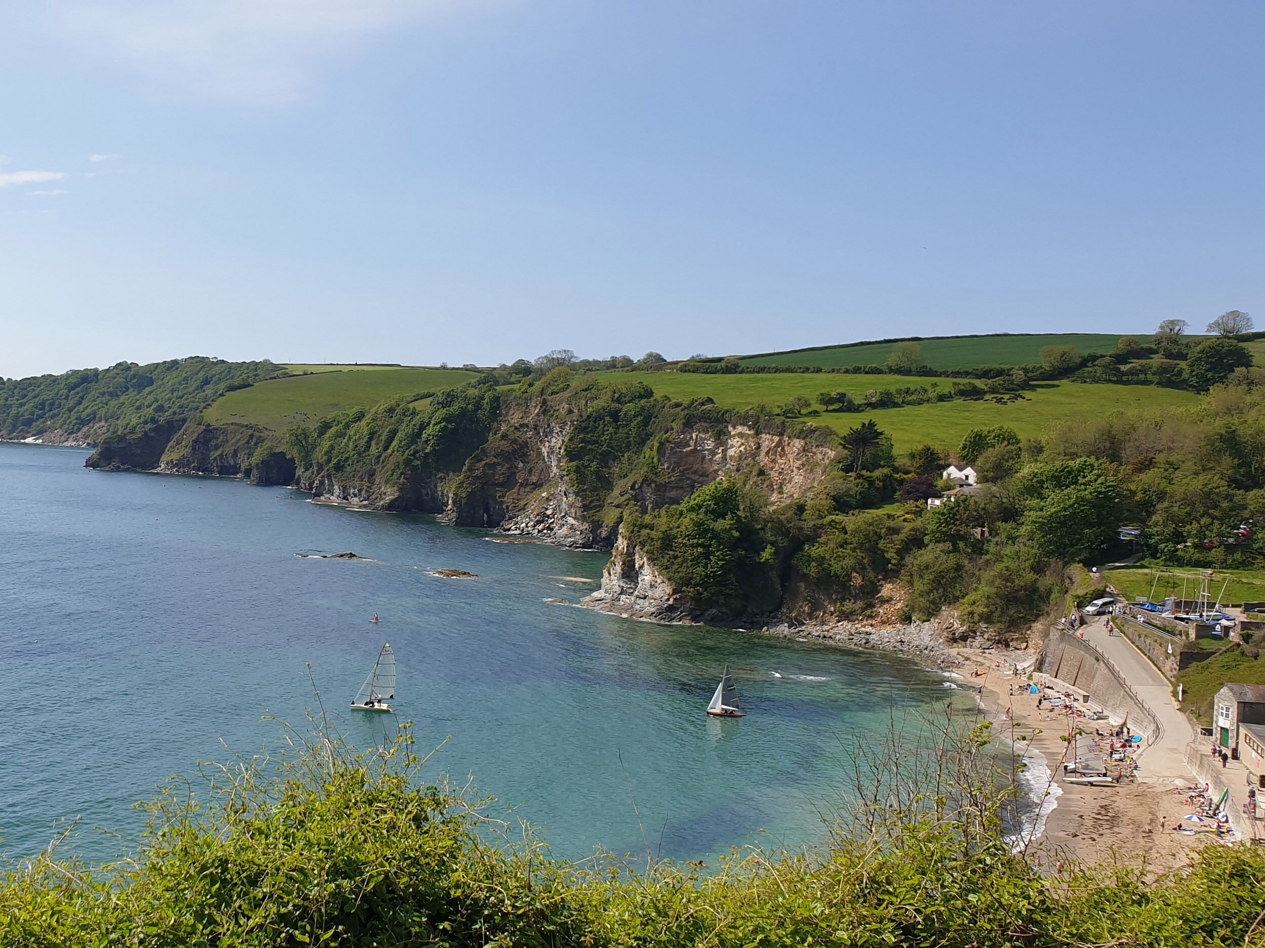 A coastal landscape with cliffs, a beach, and sailboats on the water.