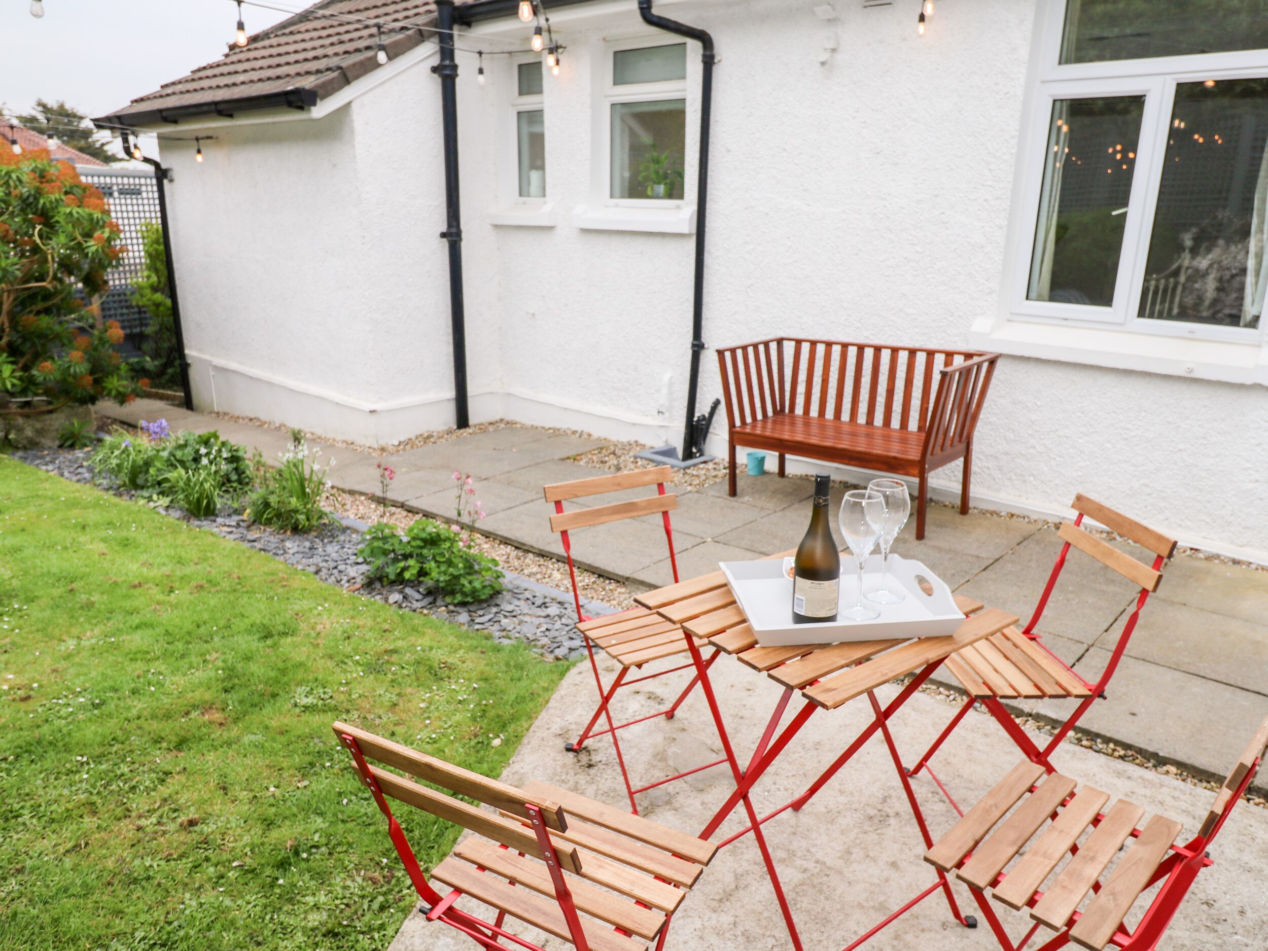 A patio with a wooden table and chairs, a bottle of wine, and a glass.