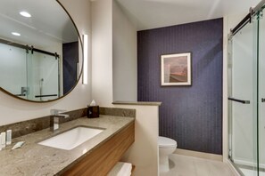 A modern bathroom with a marble sink, a large mirror, a framed picture on the wall, and a glass shower enclosure.