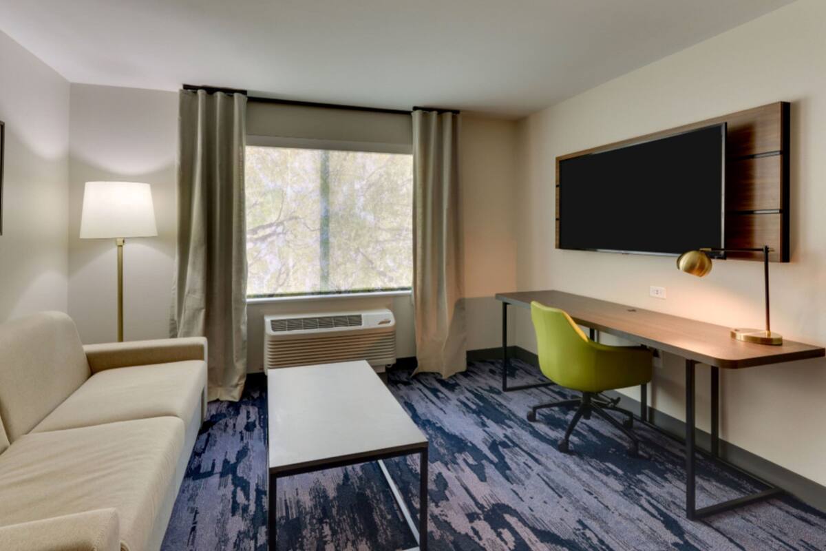 Habitación de hotel con sofá, escritorio, silla, televisión y ventana con cortinas.