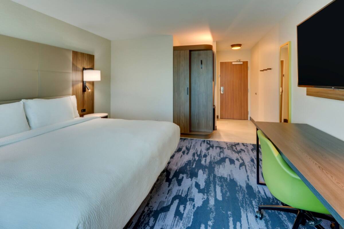 Habitación de hotel con una cama grande, un escritorio con silla, un televisor y una puerta que da a otra habitación.