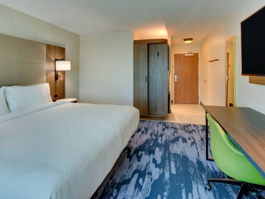 A hotel room with a large bed, a desk with a chair, a television, and a door leading to another room.