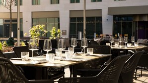 An outdoor dining area with tables set for a meal, surrounded by chairs and an umbrella. - AC Hotel by Marriott Wuerzburg (Würzburg)