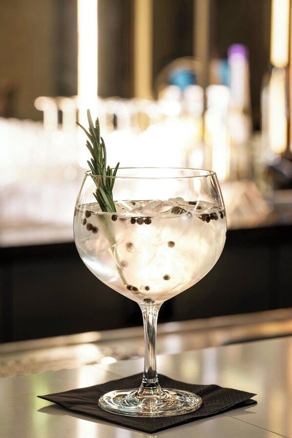 Un vaso transparente con cubitos de hielo y una ramita de romero, sobre un servilleta negra en la barra.