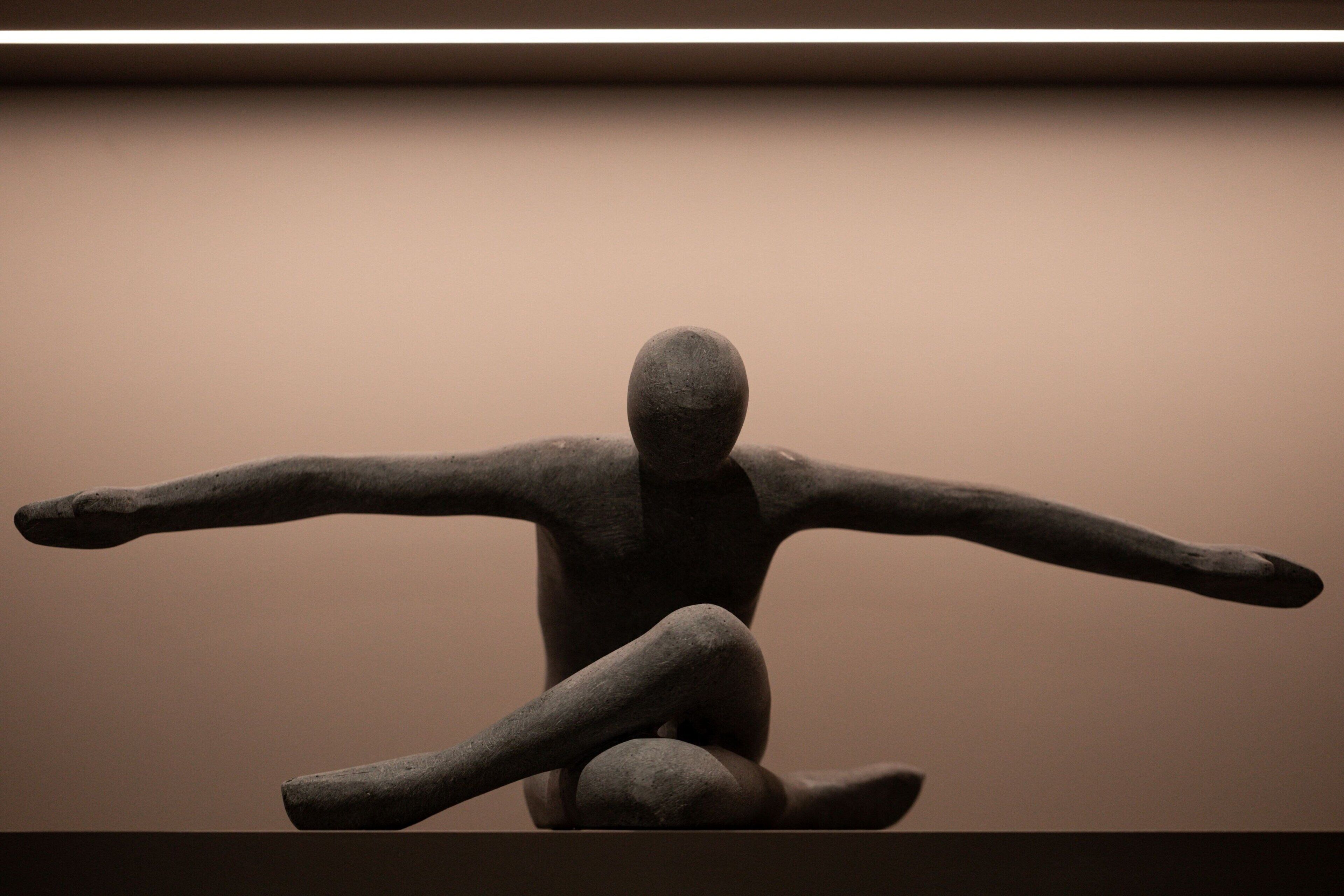 Eine Skulptur, die eine sitzende menschliche Gestalt mit ausgestreckten Armen zeigt.