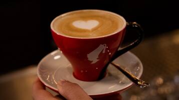 Eine Hand hält eine rote Kaffeetasse mit einem herzförmigen Muster auf dem Milchschaum, platziert auf einem Untertasse.