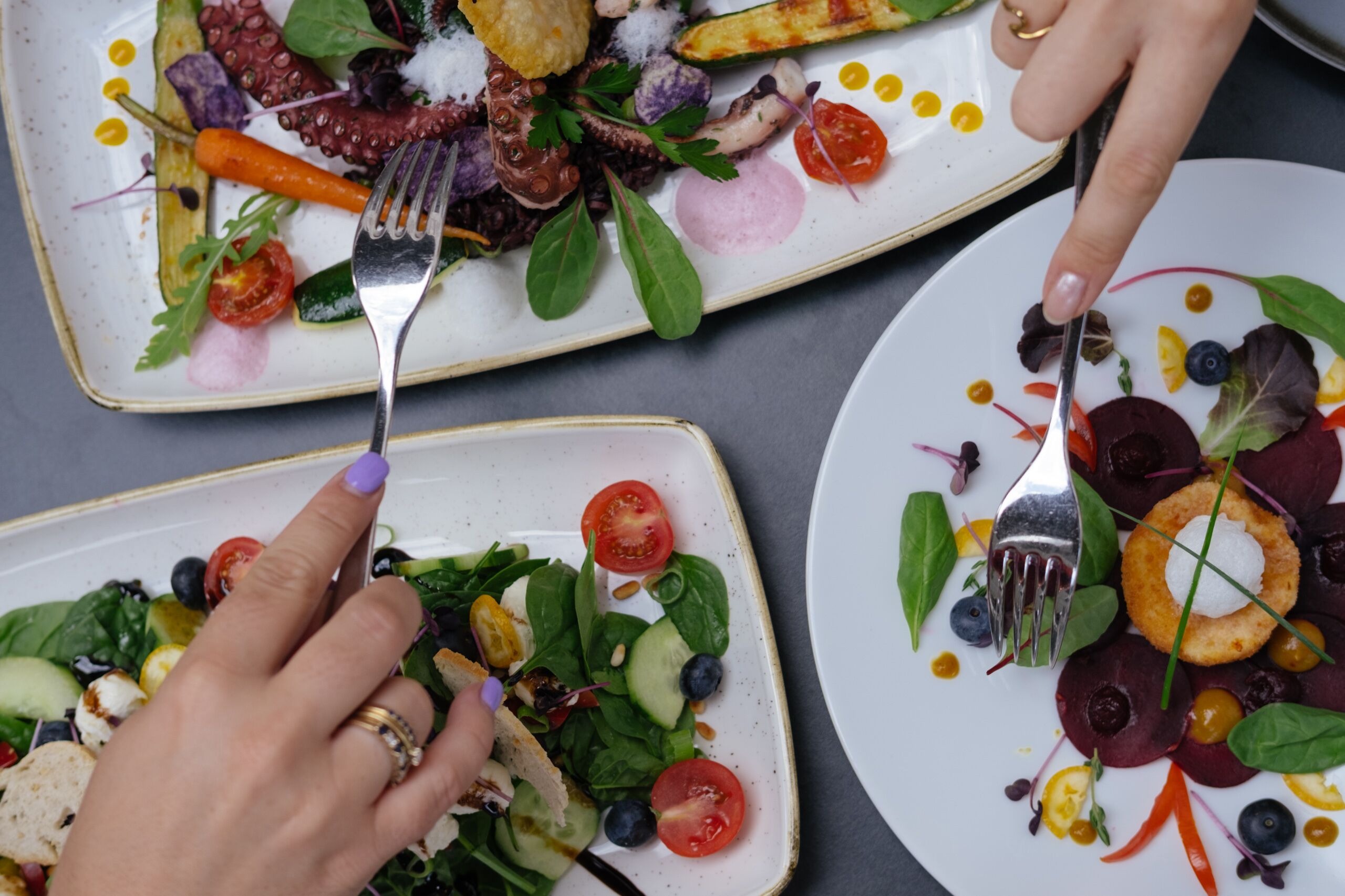 A dining table with three plates of food, each with a variety of vegetables and garnishes.