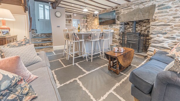 A cozy living room with a stone fireplace, a dining area with bar stools, and a kitchen in the background. - Old Toffee Shop (Ambleside)