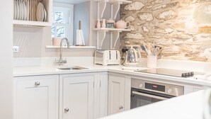 A kitchen with white cabinets, a stone wall, a toaster, a kettle, and a sink. - Old Toffee Shop (Ambleside)