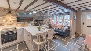 A kitchen with a stone wall, wooden beams, a built-in oven, and a bar area with stools. - Old Toffee Shop (Ambleside)