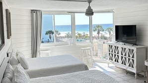 A hotel room with a large bed, a TV, a balcony with a view of the beach, and a white cabinet.