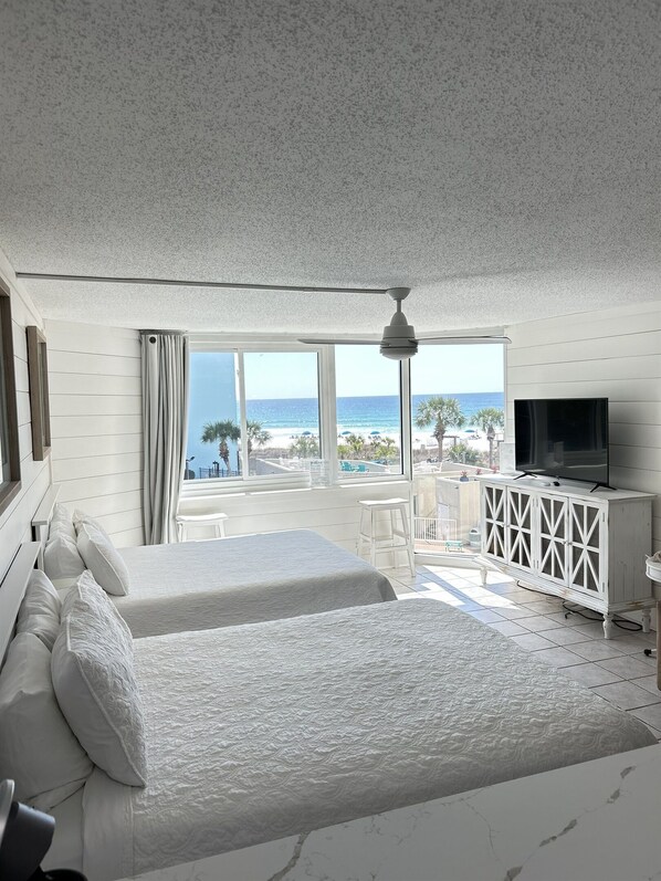 A hotel room with a large bed, a TV, a balcony with a view of the beach, and a white cabinet. - 🏖️ Affordable Cozy Beachfront | FREE Beach Chairs | Early 3PM Check-In (Panama City Beach)