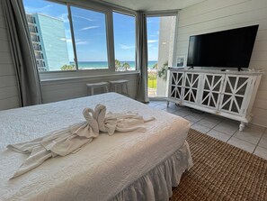 A hotel room with a bed, a TV, a white cabinet, and a view of the ocean.