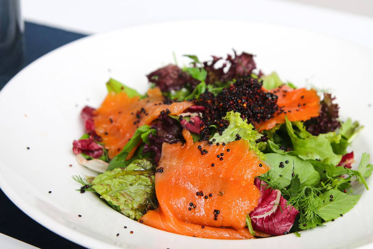 A white plate with a salad containing salmon, lettuce, and red cabbage.