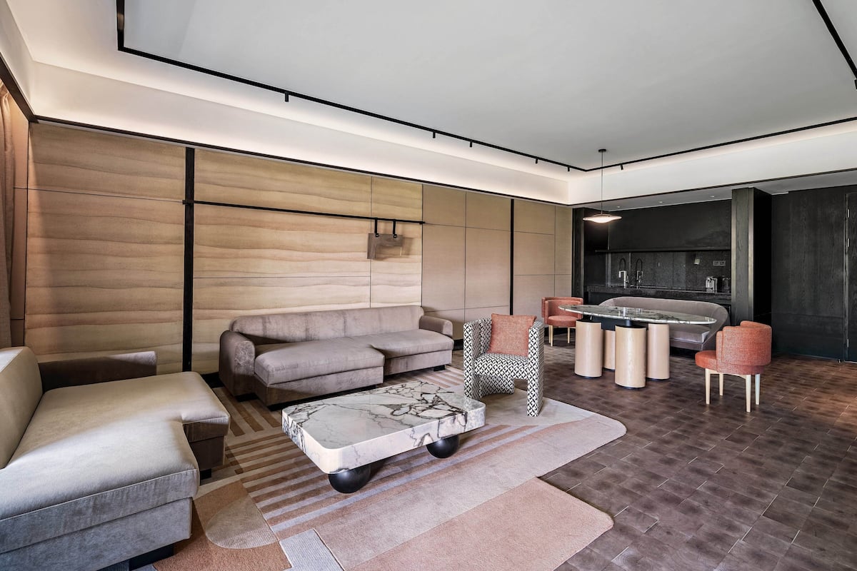 A modern living room with a sofa, armchairs, a coffee table, and a kitchen area with a dining table.