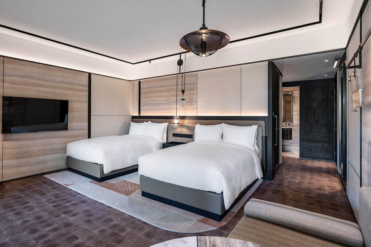 A modern bedroom with two beds, a large mirror, and a television.