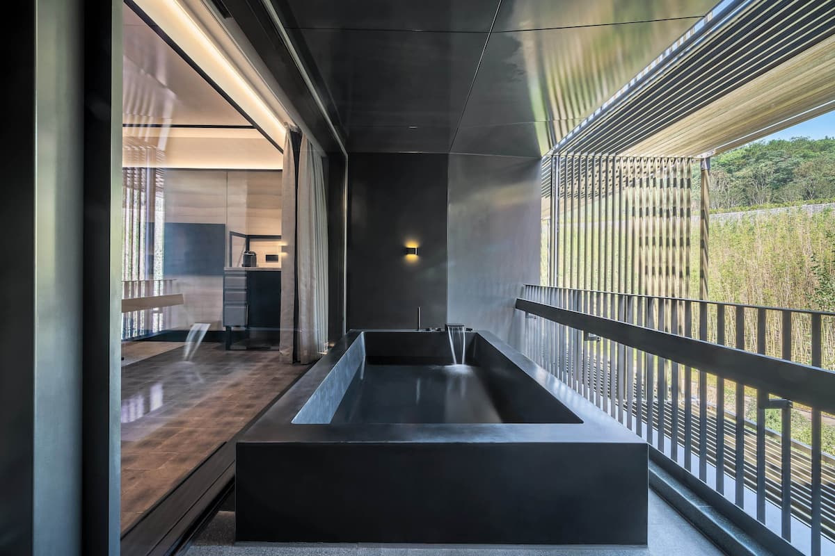 A modern interior with a long, narrow bathtub, large windows, and a view of greenery outside.