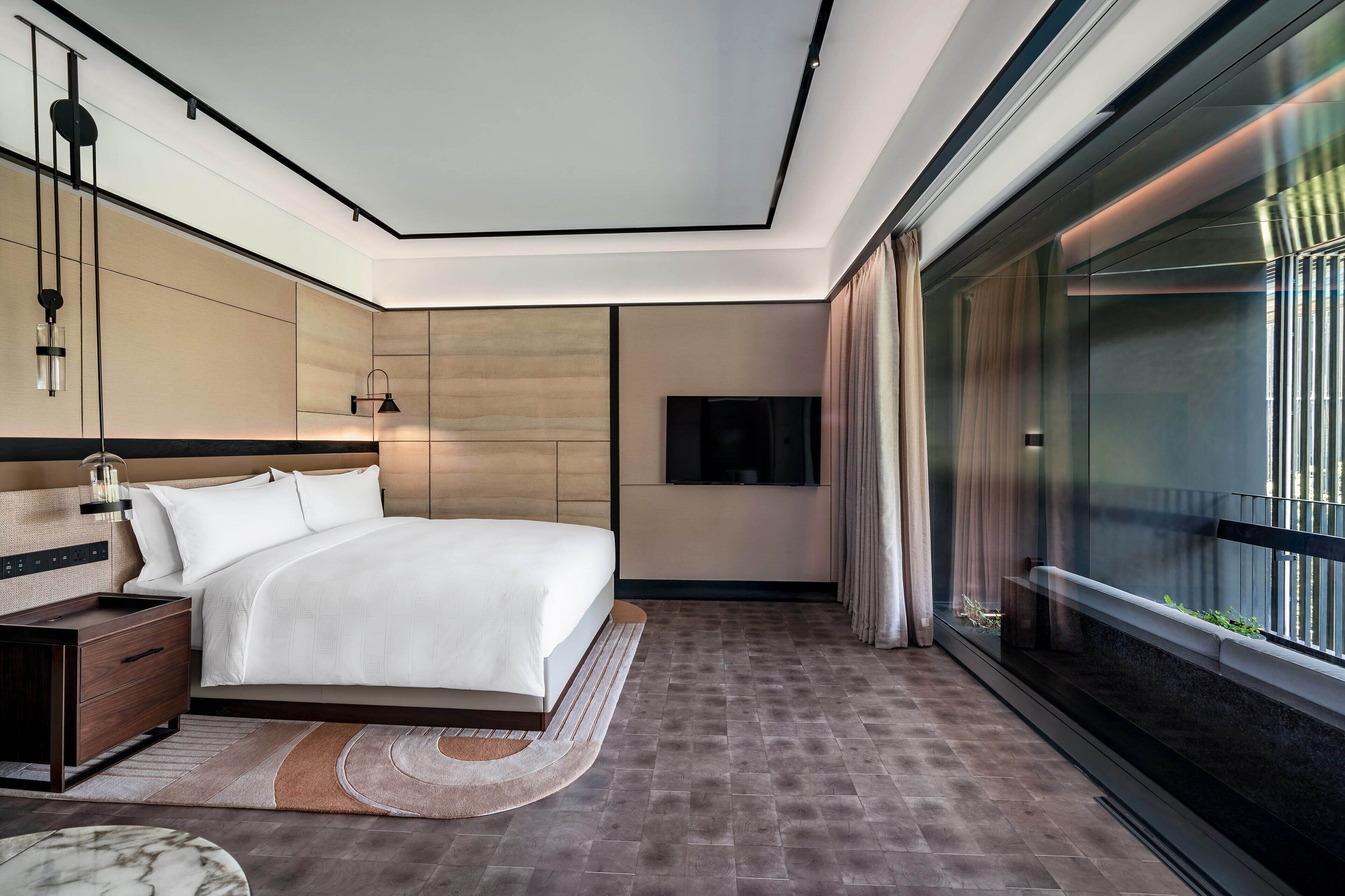 Quarto de hotel moderno com uma cama grande, uma mesa de cabeceira, televisão e varanda com vista.