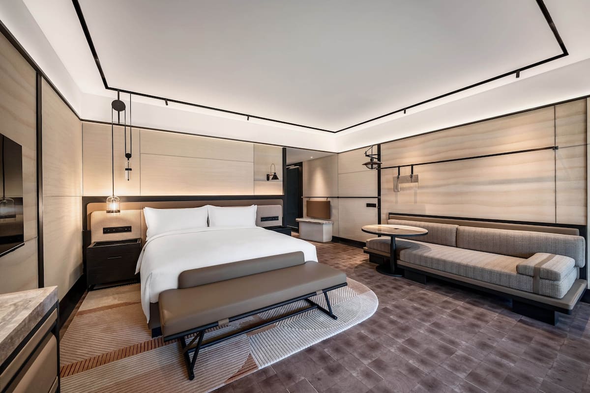 A modern hotel room with a large bed, a sofa, a small table, and a TV.