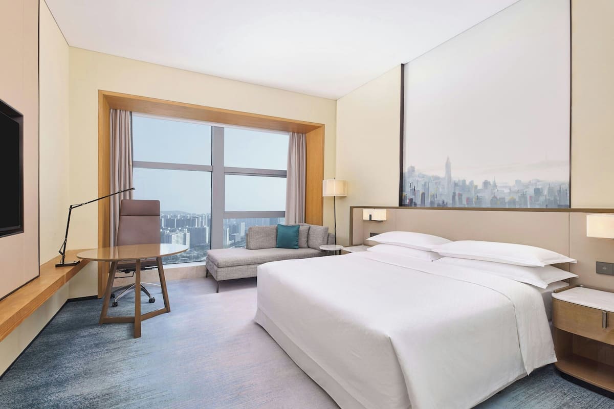 A hotel room with a large bed, a sofa, a desk, and a cityscape view.
