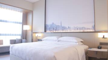 A hotel room with a large bed, a cityscape view, a bedside table with a lamp, and a window with curtains.