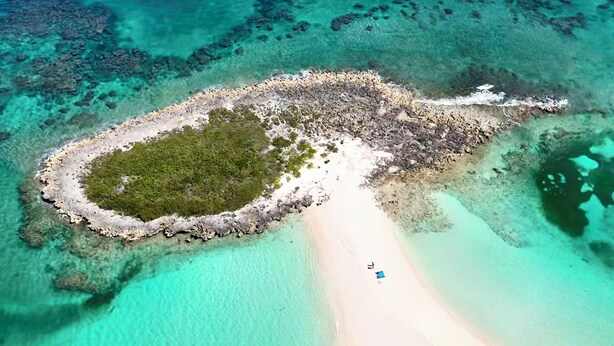 Vue aérienne d’une petite île dotée d’une plage de sable et d’eaux turquoise cristallines.