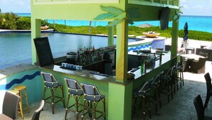 Un espace bar avec vue sur la piscine, des tabourets de bar et un toit de chaume.