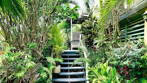 Un escalier entouré d’une végétation luxuriante, menant à une zone abritée dotée d’une rambarde.