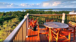 Une terrasse en bois avec une table ronde et des chaises, offrant une vue sur un paysage côtier avec la mer et des îles au loin.