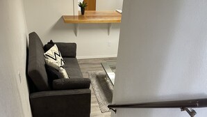 A staircase leading to a living area with a dark-colored sofa and a small plant on a wooden table.