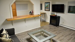 A living room with a glass coffee table, a wooden shelf, a fireplace, and a TV mounted on the wall.