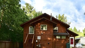 A two-story wooden cabin with a front porch, a staircase, and a small front yard.