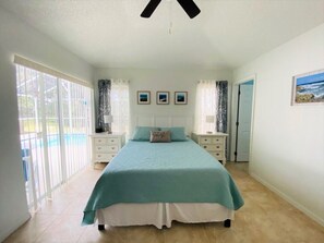 Un dormitorio con una cama grande, dos mesitas de noche, un ventilador de techo y vistas al exterior.