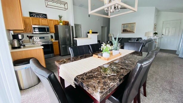 A modern kitchen with wooden cabinets, a stainless steel refrigerator, and a dining area with a marble table and black leather chairs. - Private Pool - TV in all Bedrooms - Newly renovated - Golf View (Haines City)