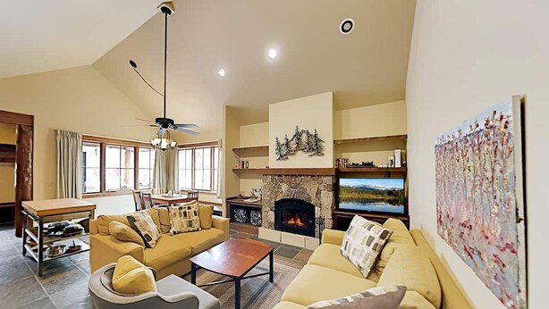 A spacious living room with a stone fireplace, a sofa, a coffee table, and a television. - Mountain Retreat | Fire Pit | 3 Blocks off Main St. (Grand Lake)