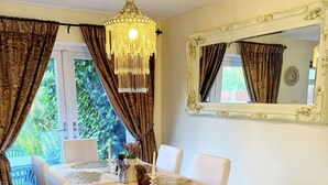 Ein Essbereich mit einem Holztisch, weißen Stühlen, einer Kristallleuchter und einem Spiegel an der Wand.
