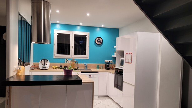 Une cuisine moderne dotée d’un îlot central, de meubles blancs, d’un mur d’accent bleu et d’une hotte en acier inoxydable.