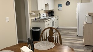 A compact kitchen with white cabinets, a sink, and a refrigerator. There is a dining table with placemats and a chair.