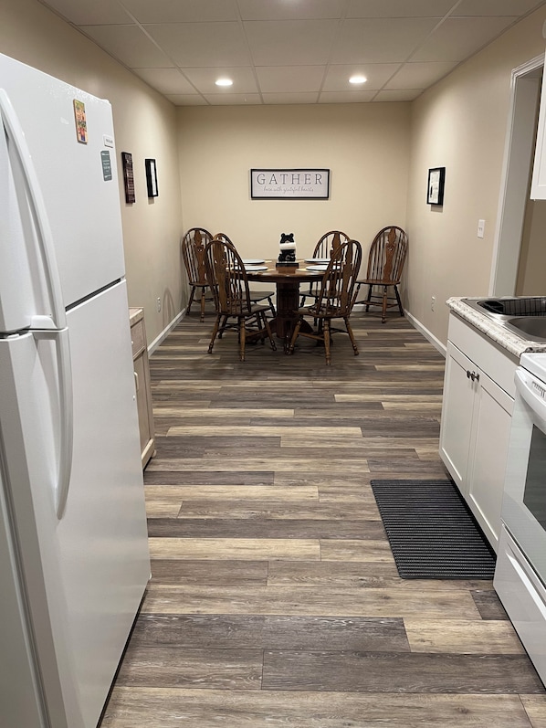 A kitchen with a white refrigerator, wooden dining table, and chairs, a kitchen island with a sink, and a herringbone-patterned floor.