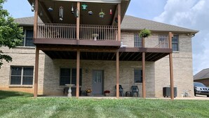 A two-story building with a covered porch, a brick exterior, and a small garden area with chairs and a bird bath.