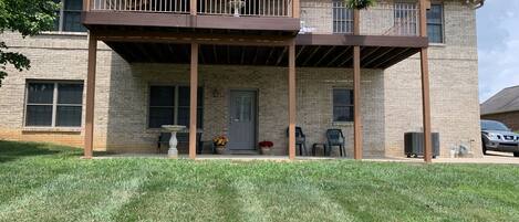 A two-story building with a covered porch, a brick exterior, and a small garden area with chairs and a bird bath.