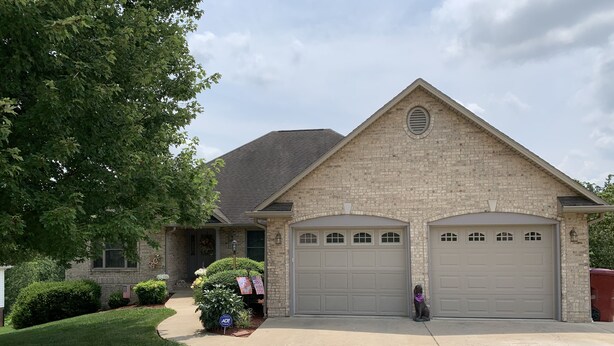 A two-story house with a brick facade, two garage doors, and a well-maintained lawn.