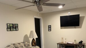 A living room with a ceiling fan, a sofa, a coffee table, and a TV mounted on the wall.