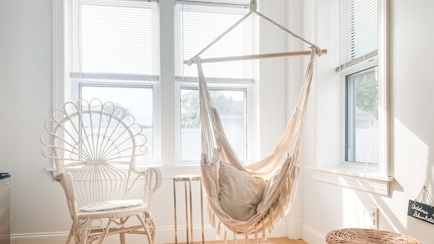 Una habitación con una silla de mimbre blanca, una hamaca colgante y una cesta tejida.