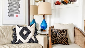 Una sala de estar con un sofá color crema, un sillón de madera, una lámpara azul y una alfombra estampada.