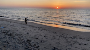Una playa con huellas que conducen al agua, un niño caminando y una puesta de sol sobre el océano.